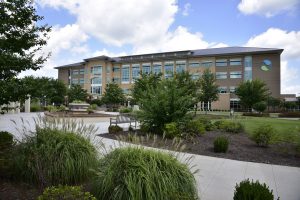 A modern, four-story hospital with large windows, green trees, gardens, benches, and a walkway under a partly cloudy sky in Georgia.