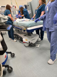 Several medical staff in blue scrubs attend to a patient in the Phoebe Worth ER, surrounded by equipment, responding quickly.