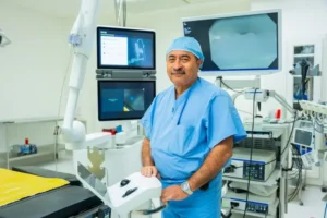 A surgeon in blue scrubs stands in an OR, raising awareness for Pulmonary Fibrosis with monitors seen behind.