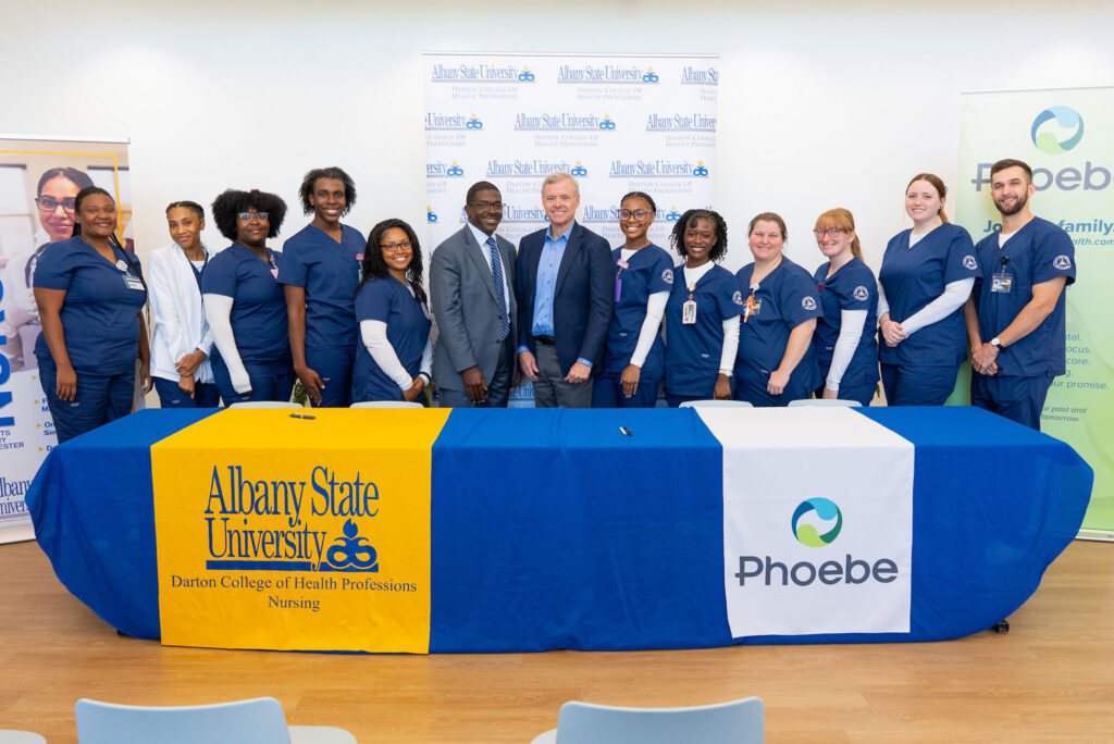 Nursing students and professionals stand behind a table for the Albany State University and Phoebe Putney nursing program
