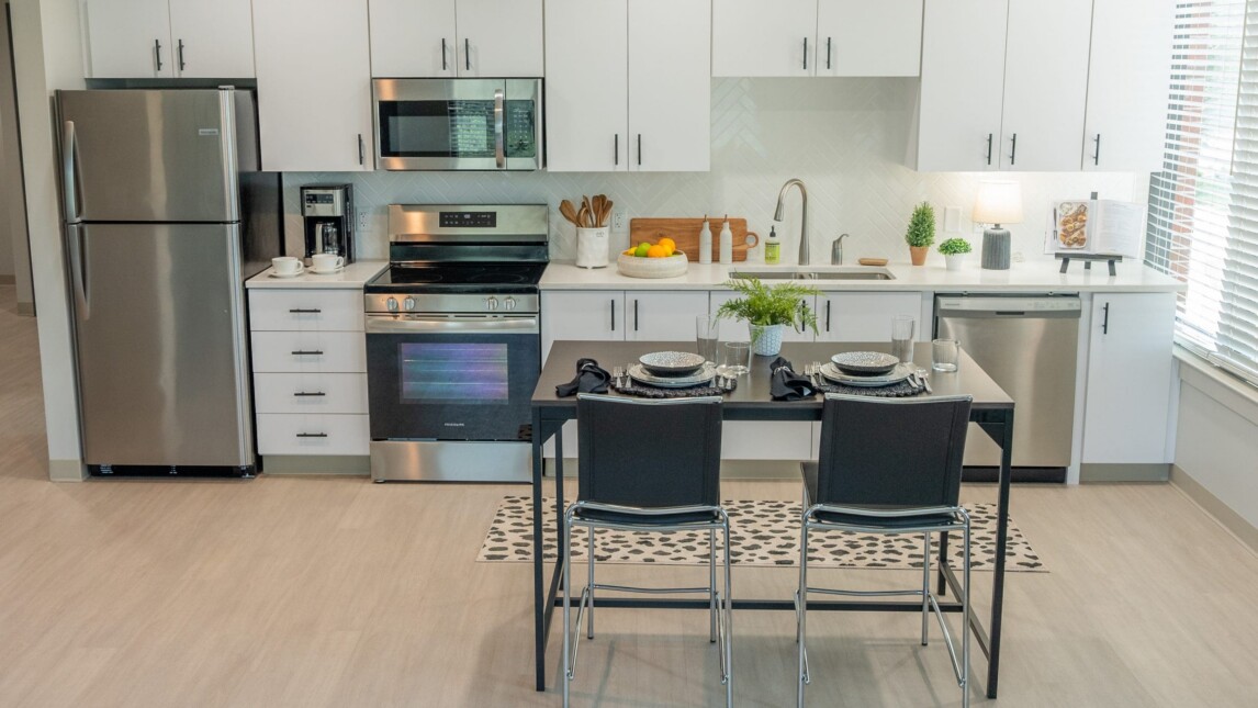 Modern kitchen with white cabinets, stainless steel appliances, and a cozy dining table for two—perfect for Living & Learning Housing. Sunlight streams in through the window, illuminating neatly arranged kitchen items on the counter. Modern kitchen with white cabinets, stainless steel appliances, and a cozy dining table for two—perfect for Living & Learning Housing. Sunlight streams in through the window, illuminating neatly arranged kitchen items on the counter.