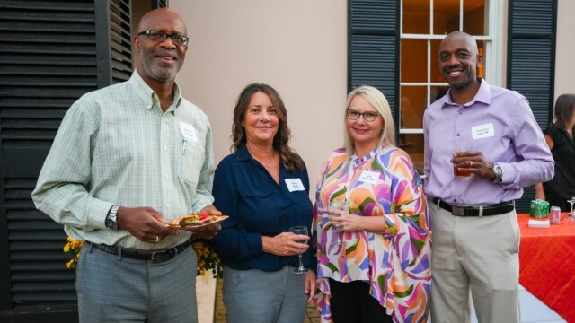 Four adults from the Phoebe Physicians Group smile at the camera during the Annual Banquet. Two men hold drinks, while two women hold wine glasses. They wear name tags, and a table with a red tablecloth sits behind them.