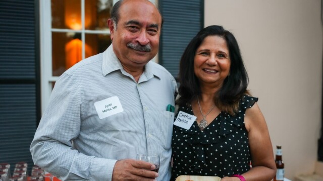 A smiling man and woman from Phoebe Physicians Group stand together at the Annual Banquet. The man holds a drink, and the woman holds a plate of food. Both wear name tags and are dressed in casual, semi-formal attire. Glasses and a bottle are nearby.