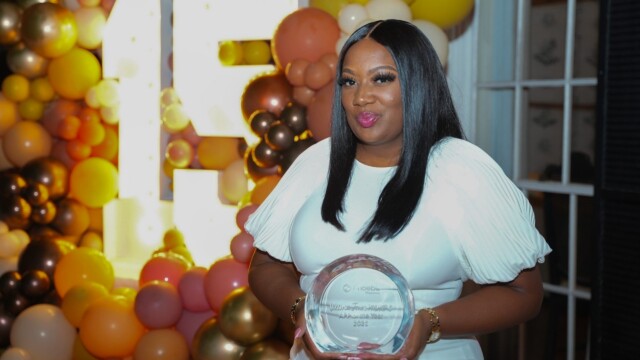 At the Annual Banquet, a woman in a white dress holds a glass award and smiles at the camera. She stands before pastel and gold balloons and a large illuminated letter F, celebrating with Phoebe Physicians Group.