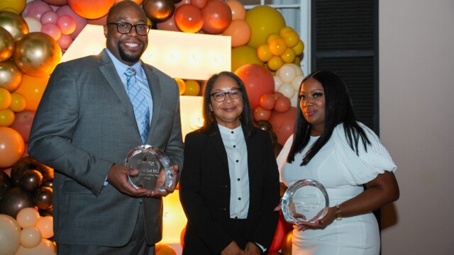 Three people smile at the Phoebe Physicians Group Annual Banquet, posing with glass awards amid colorful balloons and marquee lights.