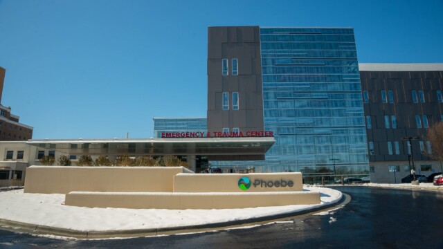 Modern hospital building with a sign reading Phoebe in front, partially surrounded by snow from a recent winter storm. The Emergency & Trauma Center entrance is visible, highlighting the hospital’s commitment to normal operations under clear blue skies.