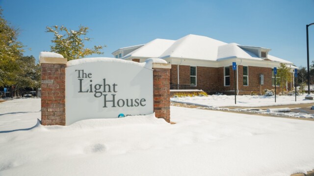 A brick building labeled “The Light House” stands amid snow-covered ground and trees under a clear blue sky, showing signs of normal operations despite the recent winter storm.